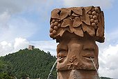 Fountain le Bacchus in sandstone on a roundabout France ; In the background: 3 castles Husseren, on the Route des Vins, near Voegtlingshoffen.