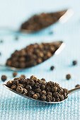 Row of teaspoons with black peppercorns on blue clothe