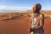 Elderly San female standing in desert landscape Namibia ; In the private reserve named "N/a’an ku sê", welfare programs and health support converge to maintain populations of Bushmen in good health and to reintroduce the wild Cheetahs. This nomadic group of hunter-gatherers has a history dating back over 20,000 years. Their close relationship and perfect their knowledge of animals allowed to live and feed in the deserts of southern Africa.