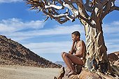 Young San girl leaning against quiver tree Namibia ; In the private reserve named "N/a’an ku sê", welfare programs and health support converge to maintain populations of Bushmen in good health and to reintroduce the wild Cheetahs. This nomadic group of hunter-gatherers has a history dating back over 20,000 years. Their close relationship and perfect their knowledge of animals allowed to live and feed in the deserts of southern Africa.