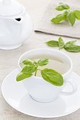 Basil tea leaves a white cup  ; Basil leaves on a work plan in stone and tea-maker in the background 