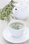 Herbal tea into a cup of white wormwood ; the leaves are put into the cup and the work plan in stone, tea-maker is placed in the background 