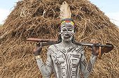 Karo warrior with body and facial paintings and a rifle in front of a hut, Omo river valley, Southern Ethiopia, Africa