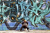 Ten-year-old boy playing with his Nintendo in front of a graffiti wall, Germany, Europe