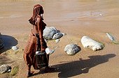 Femme himba assurant une corvée d'eau en Namibie ; Dans la région désertique ou vivent les Himbas, ce sont les femmes qui assurent l'approvisionnement en eau du village (krall) souvent à plusieurs kilomètres des points d'eau ou des rivières.