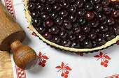 Cherries pie furnace outlet in its mold sheet , tablecloth with cherry motifs and wooden rolling pin, France
