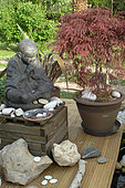 Tibetan monk statue in meditation at the edge of a Zen garden pond, Jardin de l’Écriture et de la Poésie, Garden of Writing and Poetry, Eure et Loir, France