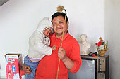 Hand pollination of pears orchards in Hanyuan, the Pear capital, Sichuan, China. In Mister Junrong's house: this former soldier, come back to his native land, poses with his young son and pollen cane. Behind him, a television and a statue of Mao date from the Cultural Revolution.