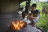 Boy heating up near the fire at dawn, Pulau Siberut, Sumatra, Indonesia