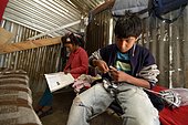 Adolescent boy, 14 years, knitting a scarf, his sister, 12 years, doing her homework, in a simple hut made of corrugated iron, Ayacucho, Ayacucho region, Peru, South America
