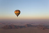 The hot-air balloon above an arid plain and isolated mountain ridges at the edge of the Namib Desert. Aerial view from a second balloon. NamibRand Nature Reserve, Namibia.