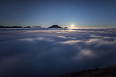 Sea of cloud and moon, night, on the Prealps. The Mole mountain and the Aravis chain emerge from the stratus, dimly lit by the moon. Alps, France
