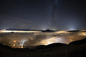 Sea of clouds lit by the Arve valley, at night, and milky way, facing the Mole mountain, the Aravis massif, and the Brasses massif. Typical autumnal stratus situation in the valleys, November 03, 2018. The clouds are illuminated by the light of the cities of the Arve. Above, the sky is clear and the Milky Way clearly visible. Scene on 180 ° (fisheye). Alps, France