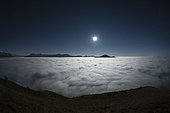 Sea of cloud and moon, night, on the Prealps. The Mole mountain and the Aravis chain emerge from the stratus, dimly lit by the moon. Alps, France