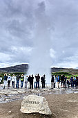 Tourists watching the gushing of a geyser: hot water coming out of the Strokkur geyser, Geysir site, Iceland.