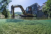 Mid-air half-water view of a digger during work to restore ecological continuity on the Lergue River, Lodève, Hérault, Occitanie region, France