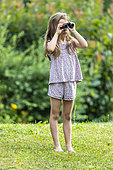 Girl watching birds in a garden with binoculars, summer, Lot, Occitanie, France