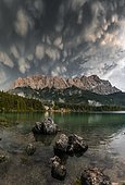 Rocks on the shore, Eibsee lake in front of Zugspitze massif with Zugspitze, sunset, dramatic Mammaten clouds, Wetterstein range, near Grainau, Upper Bavaria, Bavaria