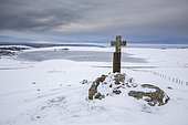 Aubrac plateau, granite cross and Lac des Moines frozen in ice, Aubrac regional natural park, Lozère, France
