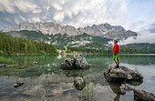 Young man standing on a rock on the shore, Eibsee lake in front of Zugspitze massif with Zugspitze, dramatic Mammaten clouds, Wetterstein range, near Grainau, Upper Bavaria, Bavaria, Germany, Europe