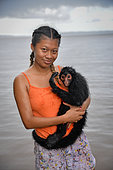 Young black spider monkey (Ateles paniscus) in the arms of a young woman in the rain in French Guiana