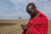 A Masai man typing a message into a mobile device. Masai Mara National Reserve, Kenya.