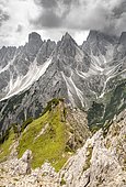 Hiker standing on a ridge, mountain peaks and pointed rocks behind, dramatic cloudy sky, Cimon di Croda Liscia and Cadini group, Auronzo di Cadore, Belluno, Italy, Europe
