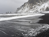 Plage de sable volcanique noir de Reynisfjara avec les stacks de Reynisdrangar après une tempête de neige. Côte de l'Atlantique Nord près de Vik y Myrdal en hiver, Terre du Sud, Islande.
