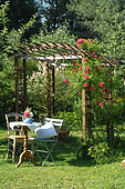 Relaxation area in the garden, wooden arbour with climbing rose Rosa 'Emera', small coffee table and chairs