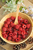 Soft fruit dessert: Raspberries and red currants from the garden in a wooden bowl, country atmosphere, table decoration: pine cones and flowers
