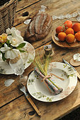 Meal in the country. Table set with bouquet of roses, bread, apricots, napkin with barley ears and cutlery with wooden handles