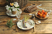 Meal in the country. Table set with bouquet of roses, bread, apricots, napkin with barley ears and cutlery with wooden handles