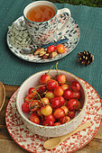 Lime infusion in plant-patterned tableware, Napoleon cherries and Brazil nuts on a country table