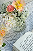 Bouquet of pink flowers, (Rosa sp) and book, relaxing in the garden, reading