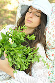 Bunch of Melissa (Melissa officinalis) and feverfew (Tanacetum parthenium), plants that promote sleep, held by a young woman lying down, sleeping in the garden