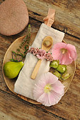 Décoration de table : assiette et cuillère en bois avec noisettes verte, figue blanche, menthe et fleurs de rose trémière, galet