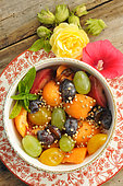 Salade de fruits d'été avec melon, raisins, prunes, pêches, menthe, graines de sarrasin, noisettes, fleur de rose trémière comestible et rose