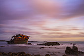 A twilight view of the wreck of the Meisho Maru No. 38, the waves and sea blurred by a long exposure, on the Cape Agulhas coastline near L'Agulhas in the Overberg, Western Cape. South Africa.