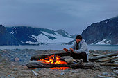 Explorateur se réchauffant les mains à la chaleur des flammes, le feu vient des nombreux bois de flottage, Ile Raffles, Terre de Liverpool, Nord Est Groenland