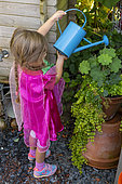 Girl watering a potted plant in summer, Moselle, France