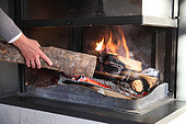 Hand putting a log in a fireplace with insert