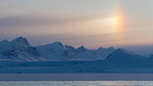 Landscape of snow-capped mountains, fixed pack ice and sky adorned with a parhelion at the bottom of Ymerbukta fjord, Spitsbergen, Svalbard archipelago.