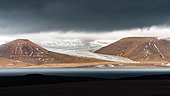 Landscape of glacier and mountains under a low, dark sky in the North-East Land of the Svalbard archipelago.