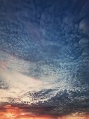 Dreamlike sunset sky vertical background with fluffy and colorful cirrus clouds above the horizon. Sunrise celestial view