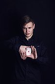 Confident young man showing tricks with playing cards like a magician, isolated on dark background. Gambling games winner, successful gambler showing illusions