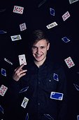 Successful young man holds up a victory lucky card. Gambler play luck games and win, isolated on dark background. Gambling jackpot winner with an ace of hearts under a rain of playing cards