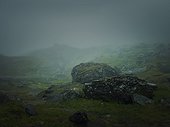 Big mountain rocks and boulders seen through the dense mist. Moody hiking scene with rainy weather