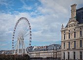 Grande Roue de Paris ferris wheel next to Louvre museum building and parisian houses, France