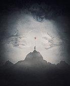 Spooky scene with a lone boy holding a red balloon on top of a mountain facing a mysterious creature with giant scary hands coming out of the fog. Fantasy adventure and thrill background