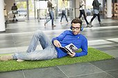 Businessman listening to music and reading book while relaxing on grass mat in an office lobby